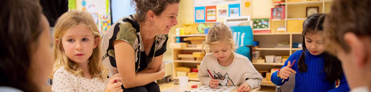Een lerares begeleidt kinderen tijdens een creatieve activiteit in de klas van een basisschool.