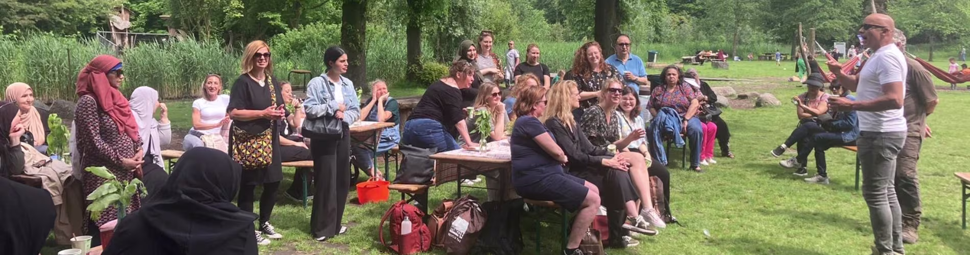 Een groep medewerkers zit ontspannen op banken in een park terwijl een man een presentatie geeft tijdens een bedrijfsuitje.