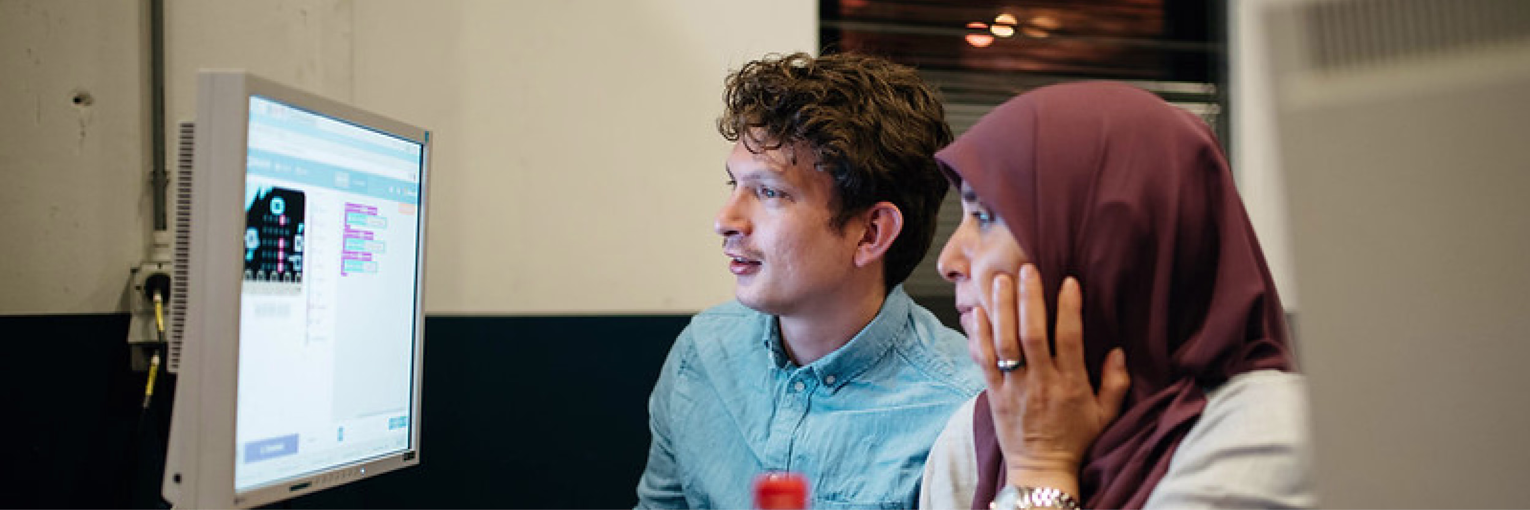 Twee collega's kijken samen naar een computerscherm en bespreken hun werk in een moderne kantooromgeving.