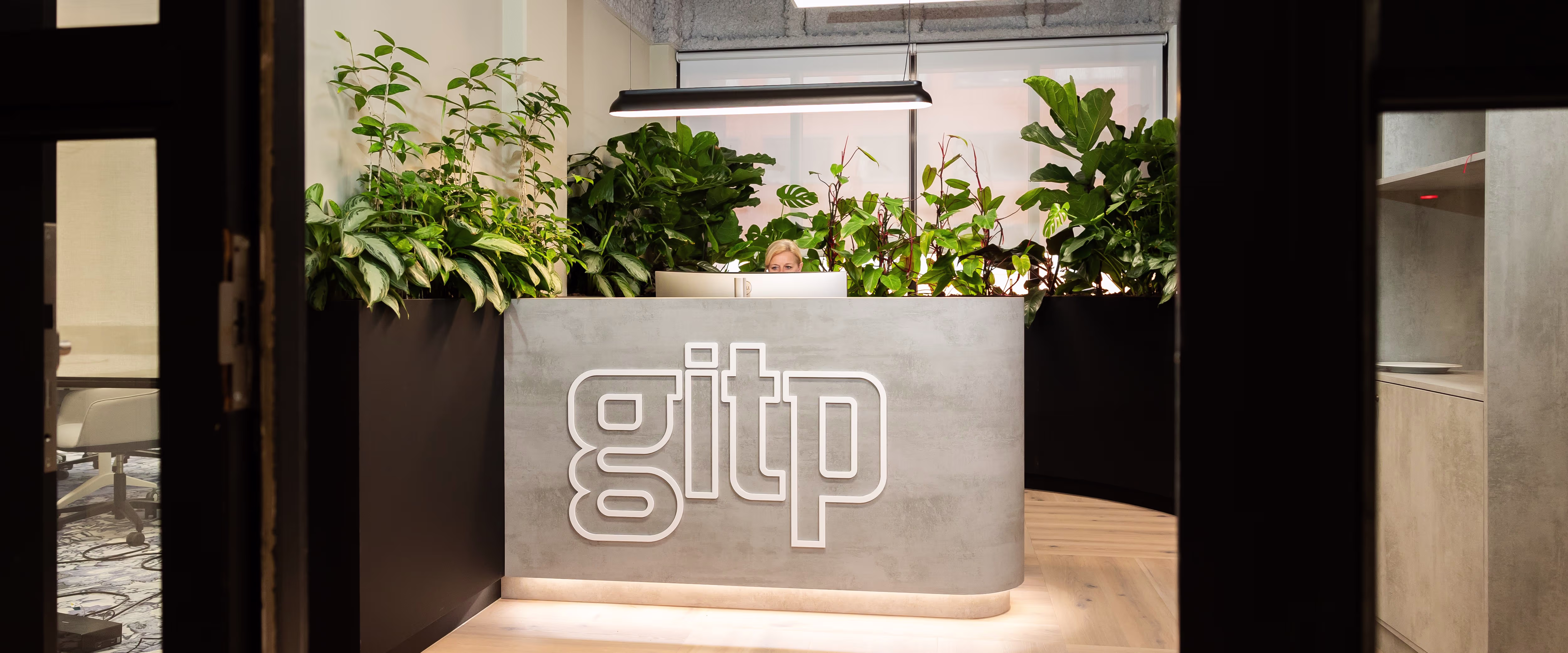 Moderne receptiebalie van GITP met groene planten en verlichte logo in strak kantoorinterieur.