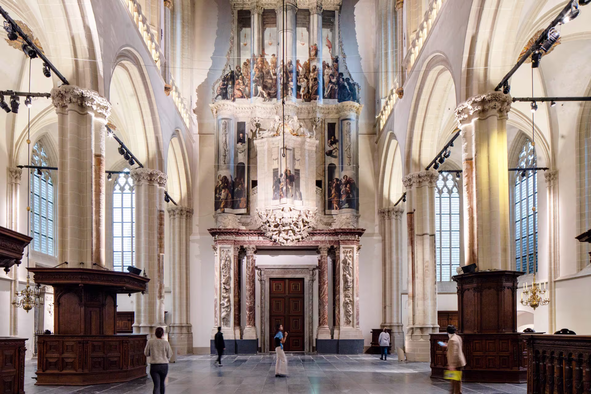 Interieur van De Nieuwe Kerk met gotische zuilen, historische preekstoel en bezoekers die door de ruimte wandelen.