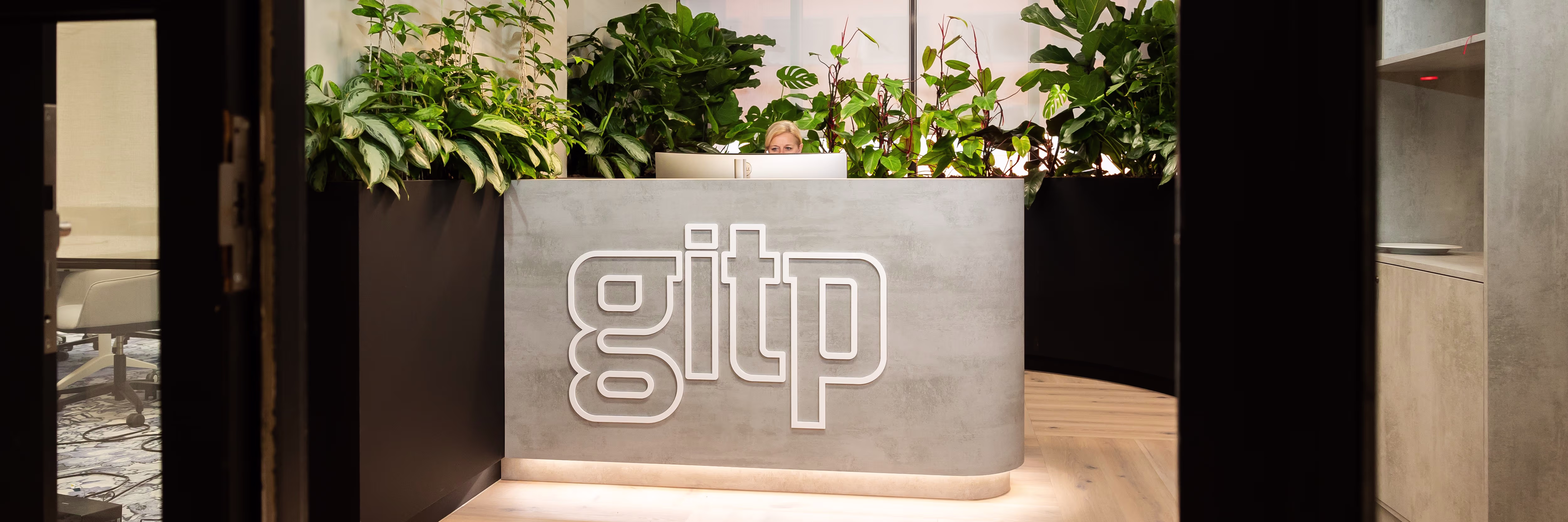 Moderne receptiebalie met het GITP-logo en groene planten erachter in een strak kantoorinterieur.
