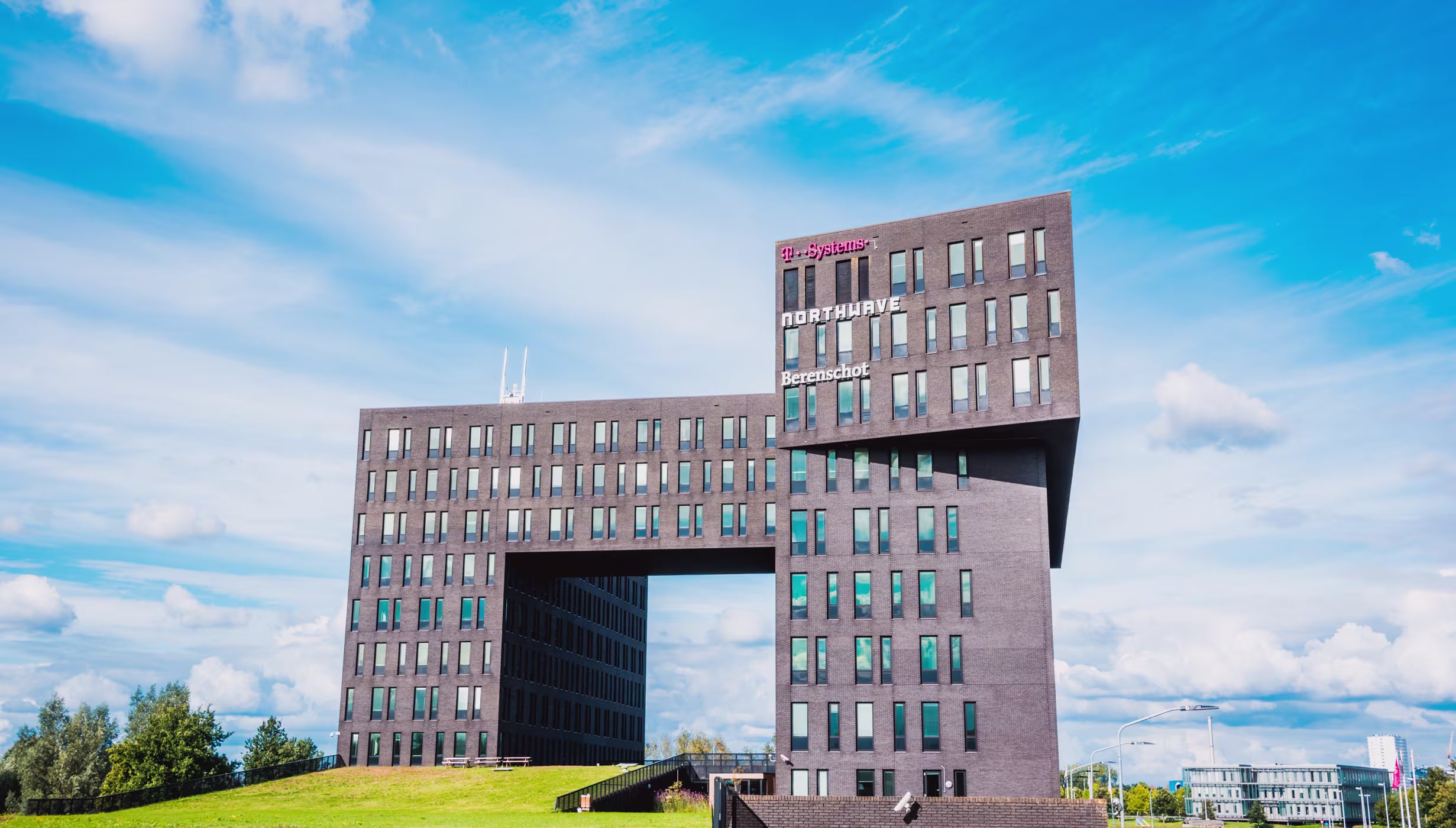 Modern kantoorgebouw van Berenschot met opvallende architectuur tegen blauwe hemel met wolken.
