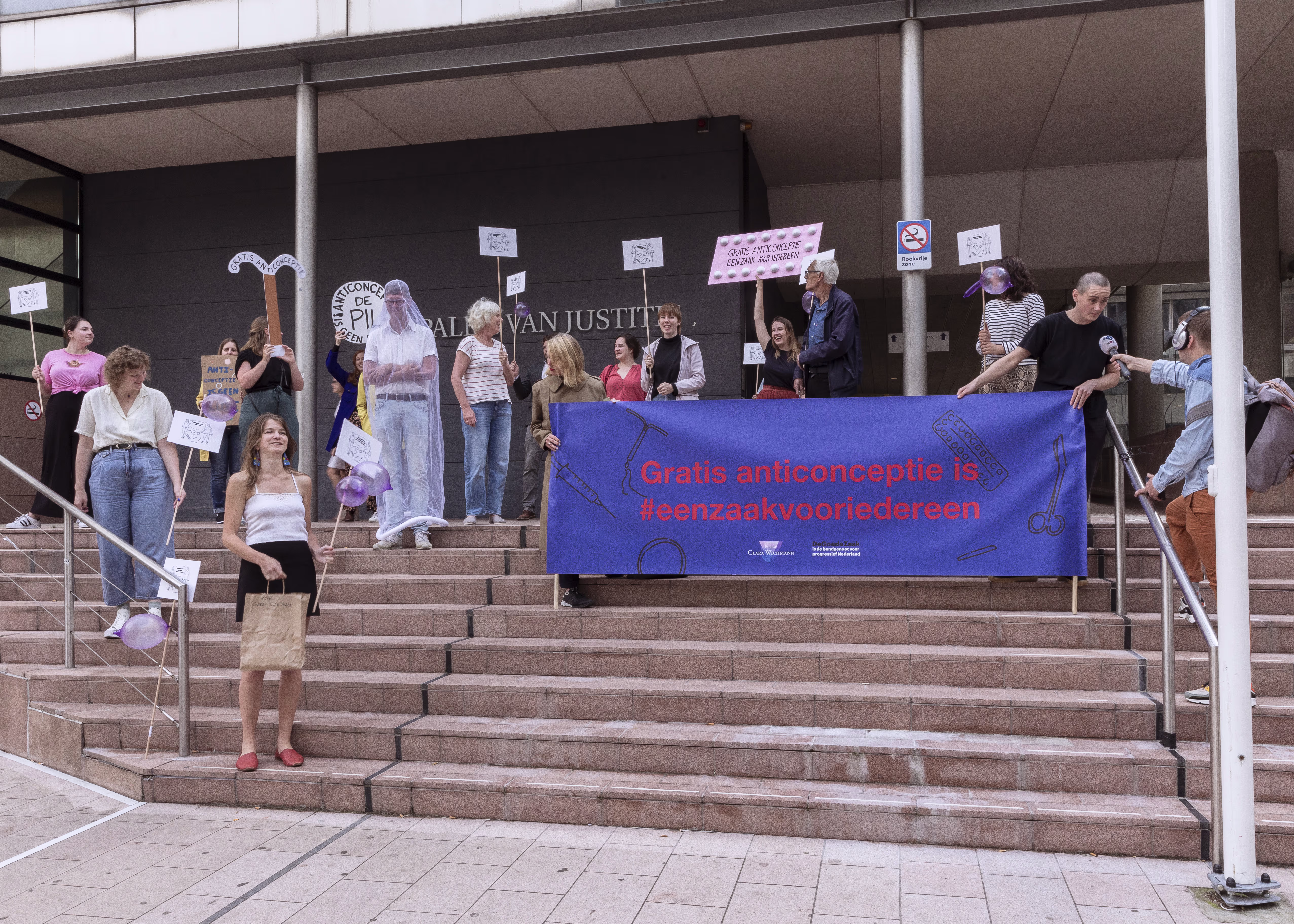 Groep demonstranten op trappen van overheidsgebouw met spandoek "Gratis anticonceptie is #eenzaakvooriedereen".