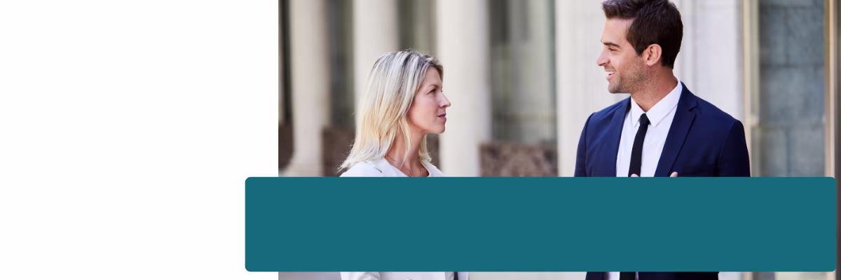 Blonde vrouw en man in donker pak kijken elkaar glimlachend aan voor een gebouw met zuilen.