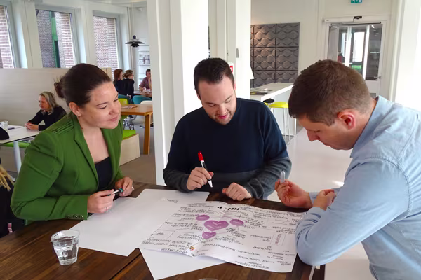 Drie collega's werken samen aan een groot vel papier met tekeningen en aantekeningen tijdens een brainstormsessie op kantoor.
