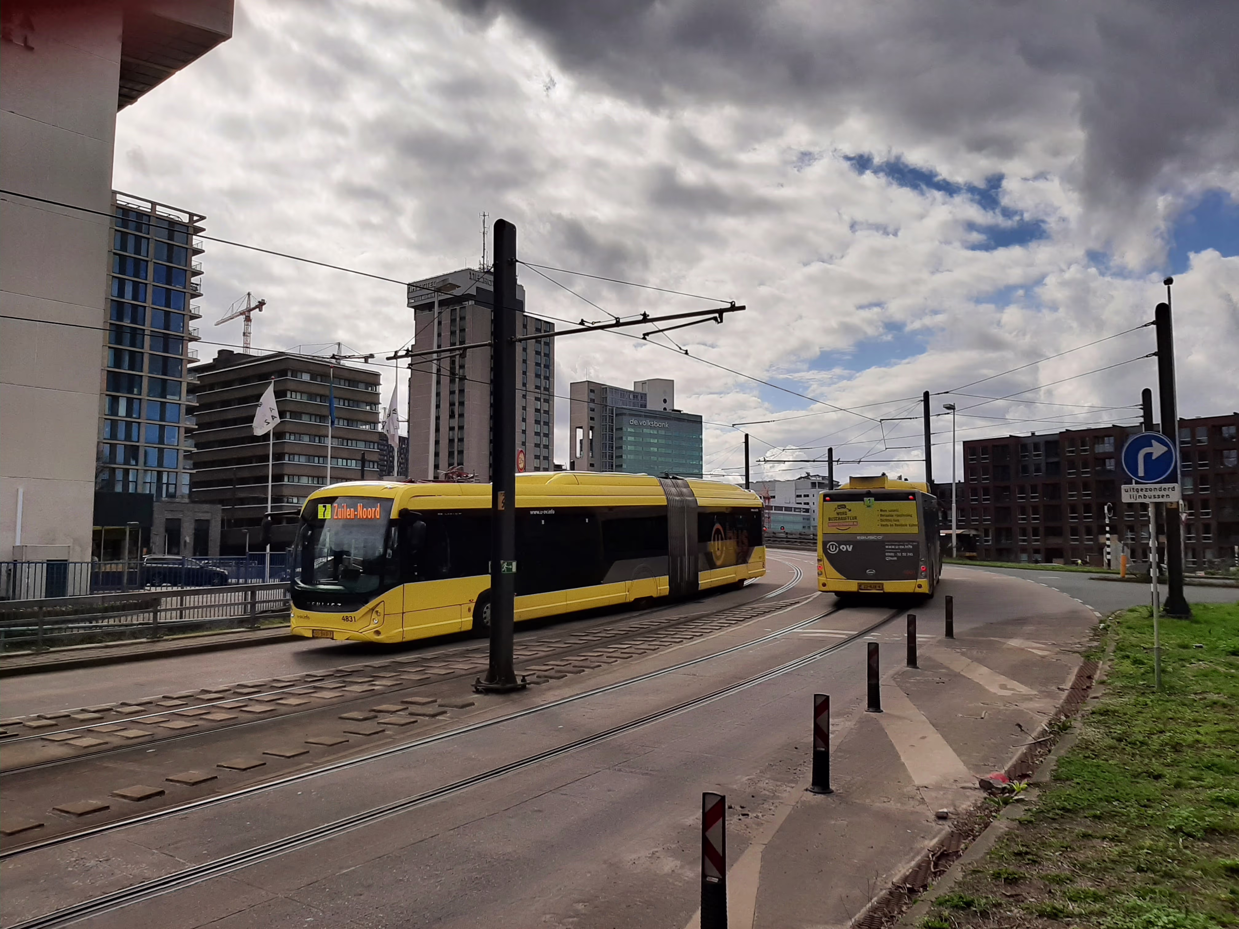 Moderne gele trams rijden door een stedelijk gebied met hoogbouw en kantoorgebouwen op de achtergrond.