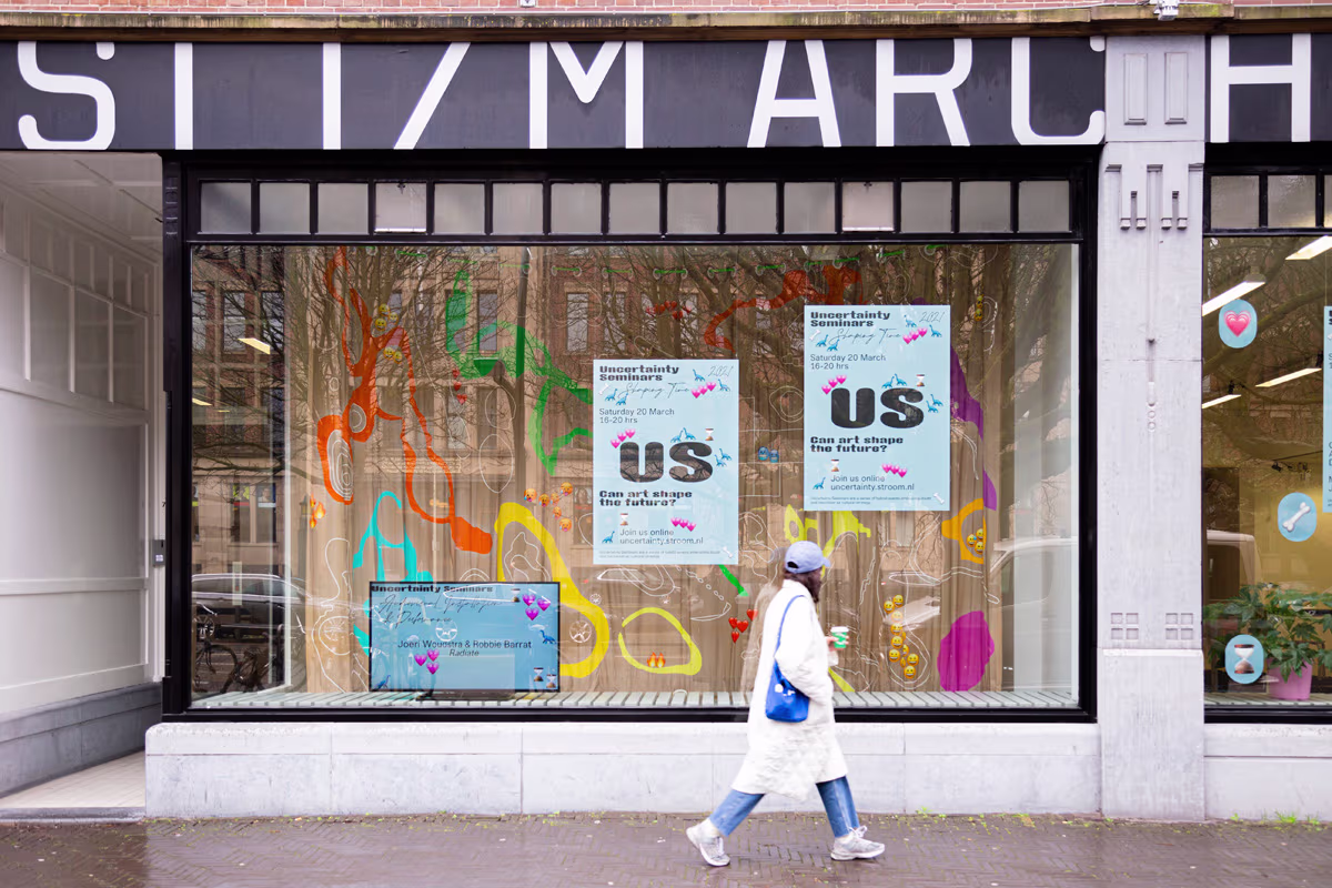 Een persoon loopt langs de etalage van Stroom Den Haag, een kunstcentrum met kleurrijke raamtekeningen en posters.