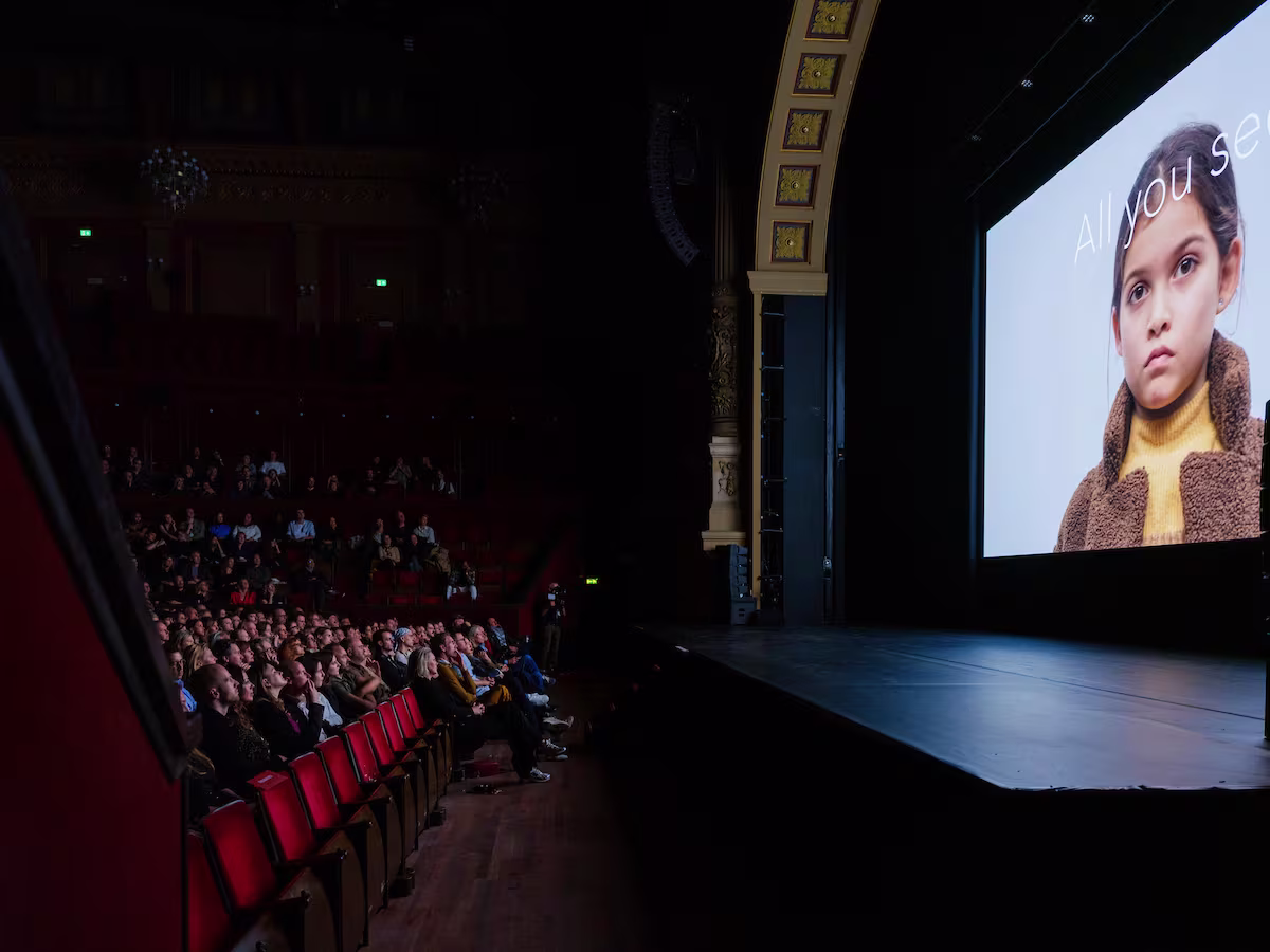 Een volle bioscoopzaal met rode stoelen waar het publiek naar een grote filmprojectie kijkt tijdens een filmfestival.