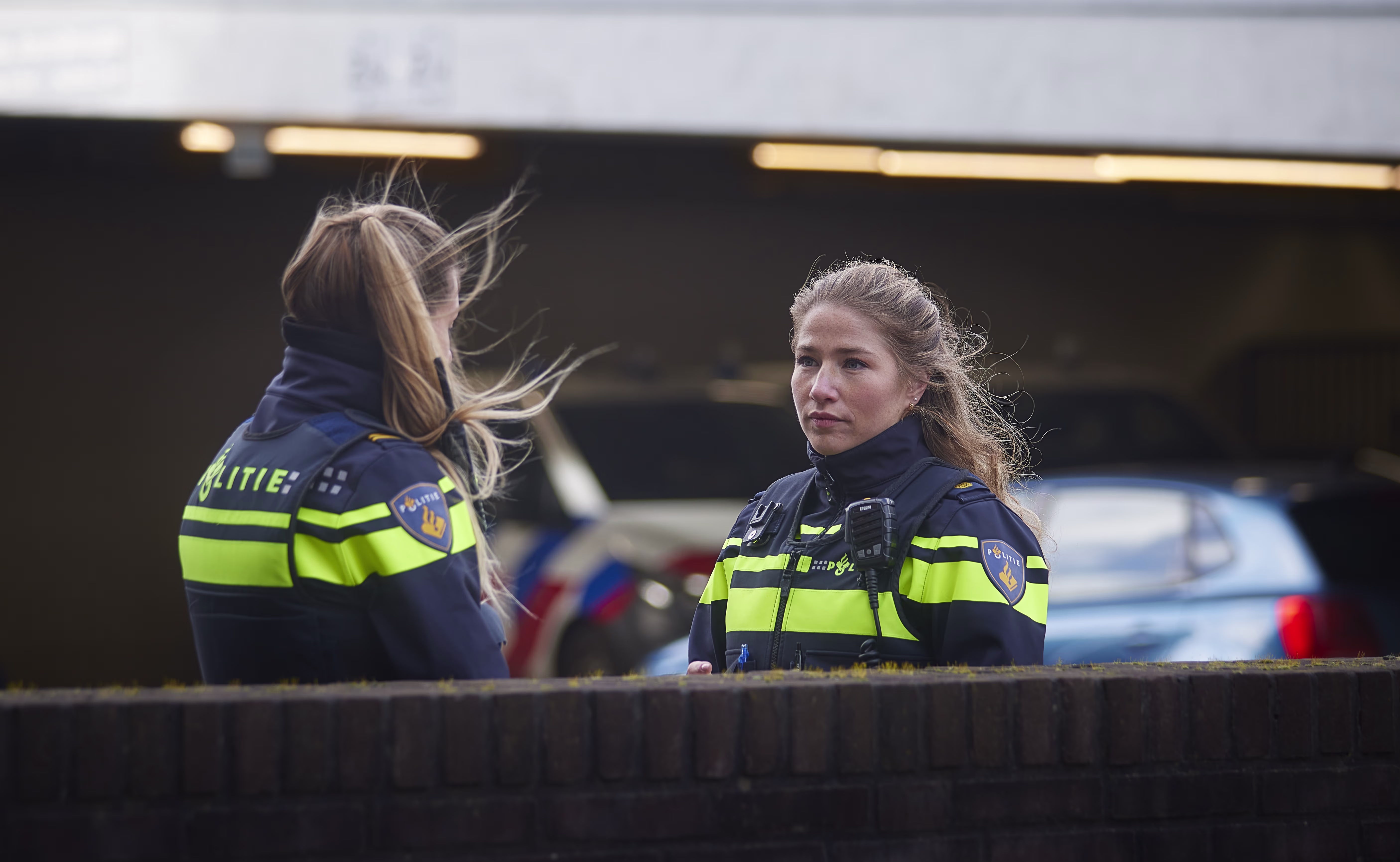 Twee vrouwelijke politieagenten in uniform staan buiten bij politieauto's en praten met elkaar.
