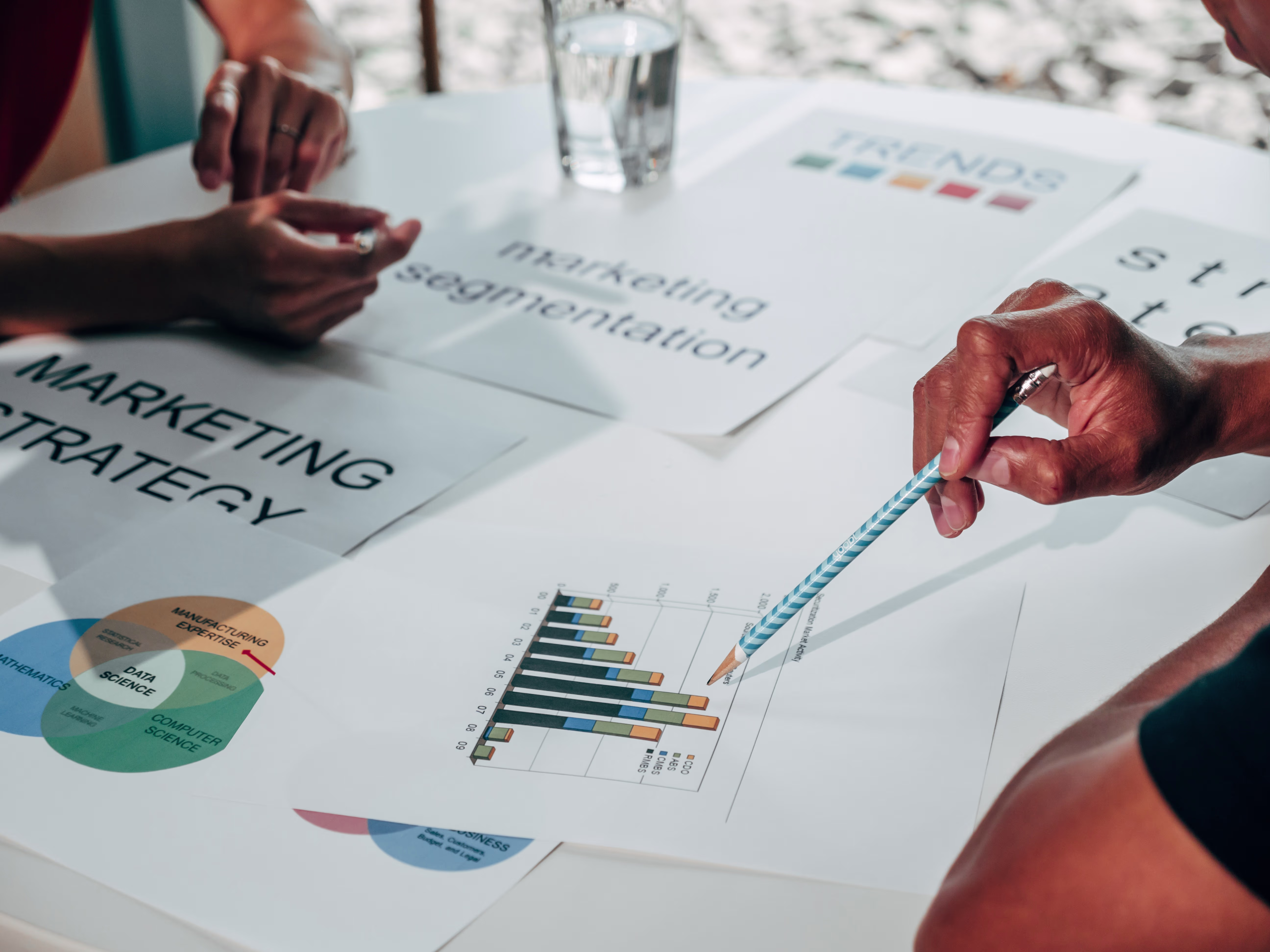 Mensen bespreken marketingstrategie aan tafel met grafieken, documenten en een glas water.