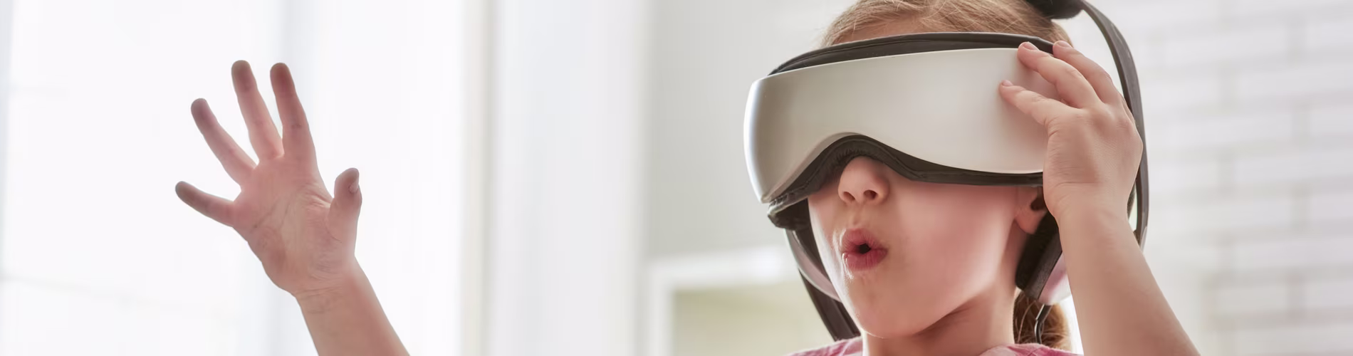 Kind gebruikt VR-bril en steekt hand uit, ervaart virtuele realiteit in helder verlichte ruimte.