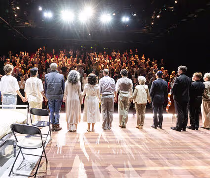 Acteurs op toneel buigen voor applaudisserende toeschouwers in een theater na een voorstelling.