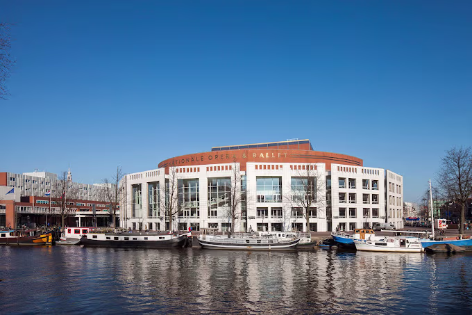 Het imposante gebouw van De Nationale Opera & Ballet aan het water in Amsterdam, met boten ervoor op een zonnige dag.