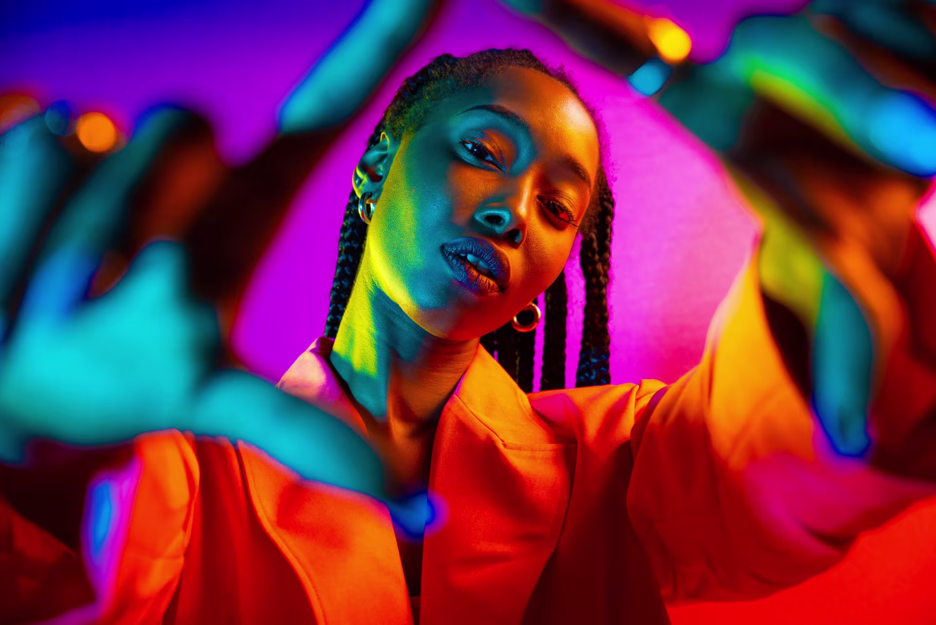 Jonge vrouw met vlechten danst uitgelaten onder kleurrijke neonverlichting in paars, oranje en blauw.