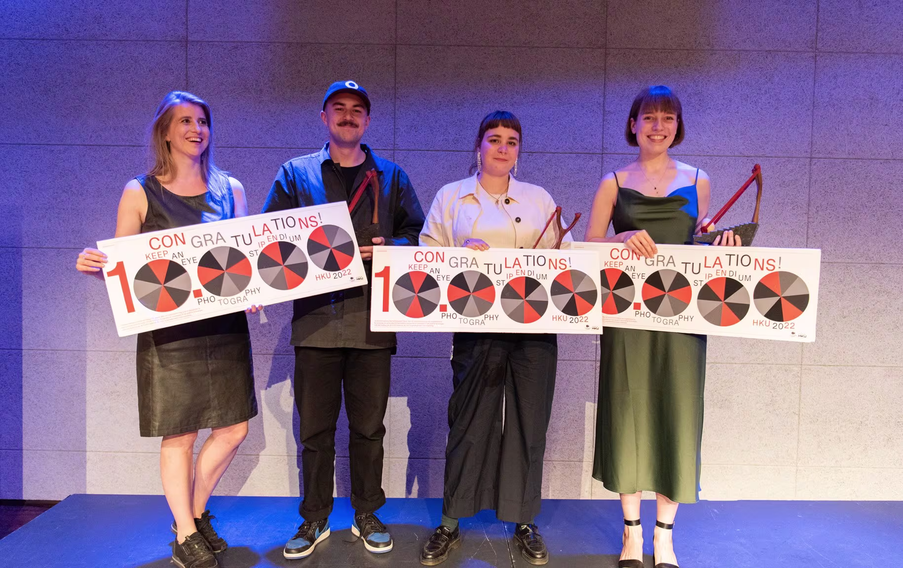 Vier afgestudeerden poseren met diploma's of certificaten op een podium tijdens een uitreiking.
