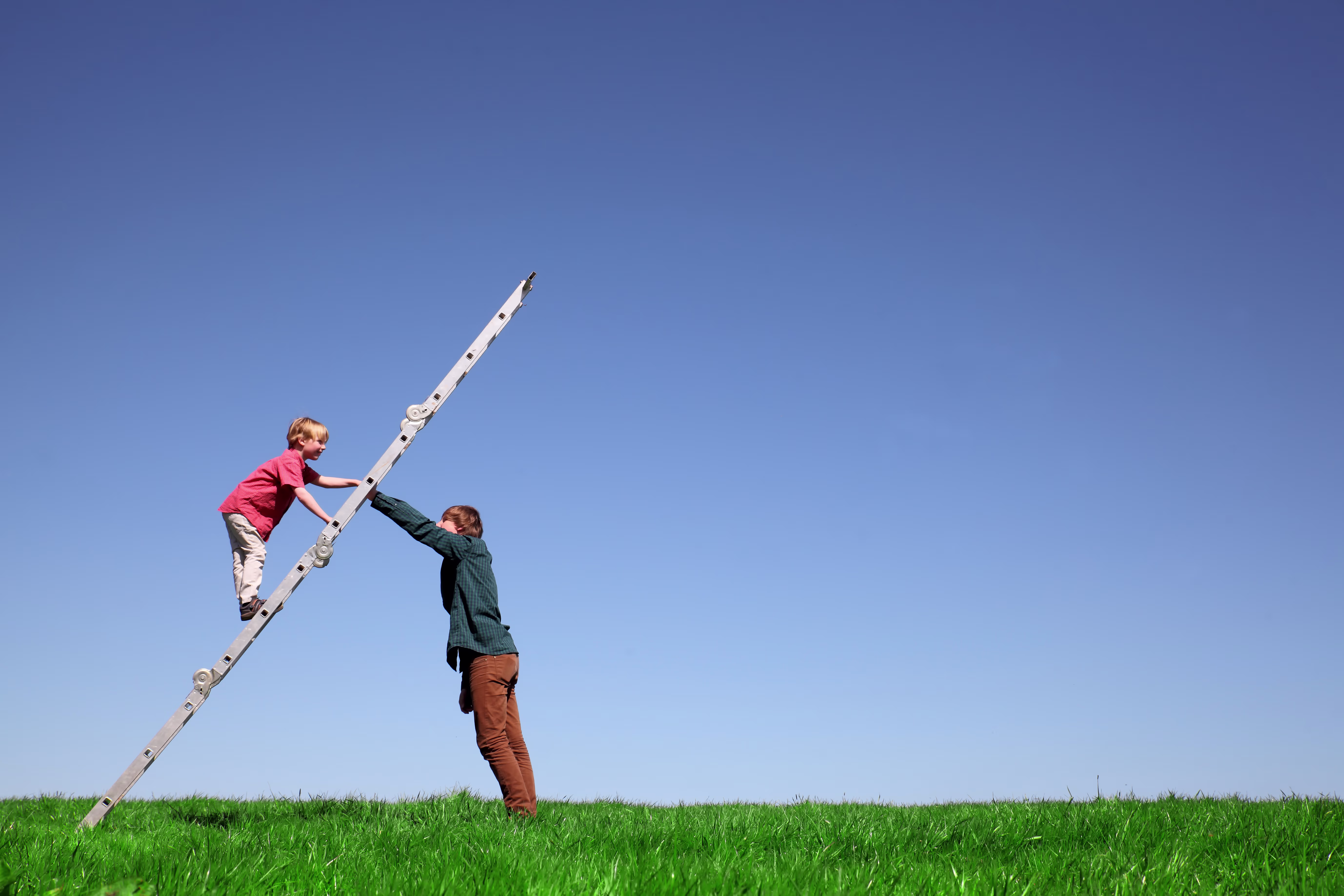 Twee personen werken samen met een ladder op een groen veld onder blauwe hemel, symboliserend teamwork en samenwerking.