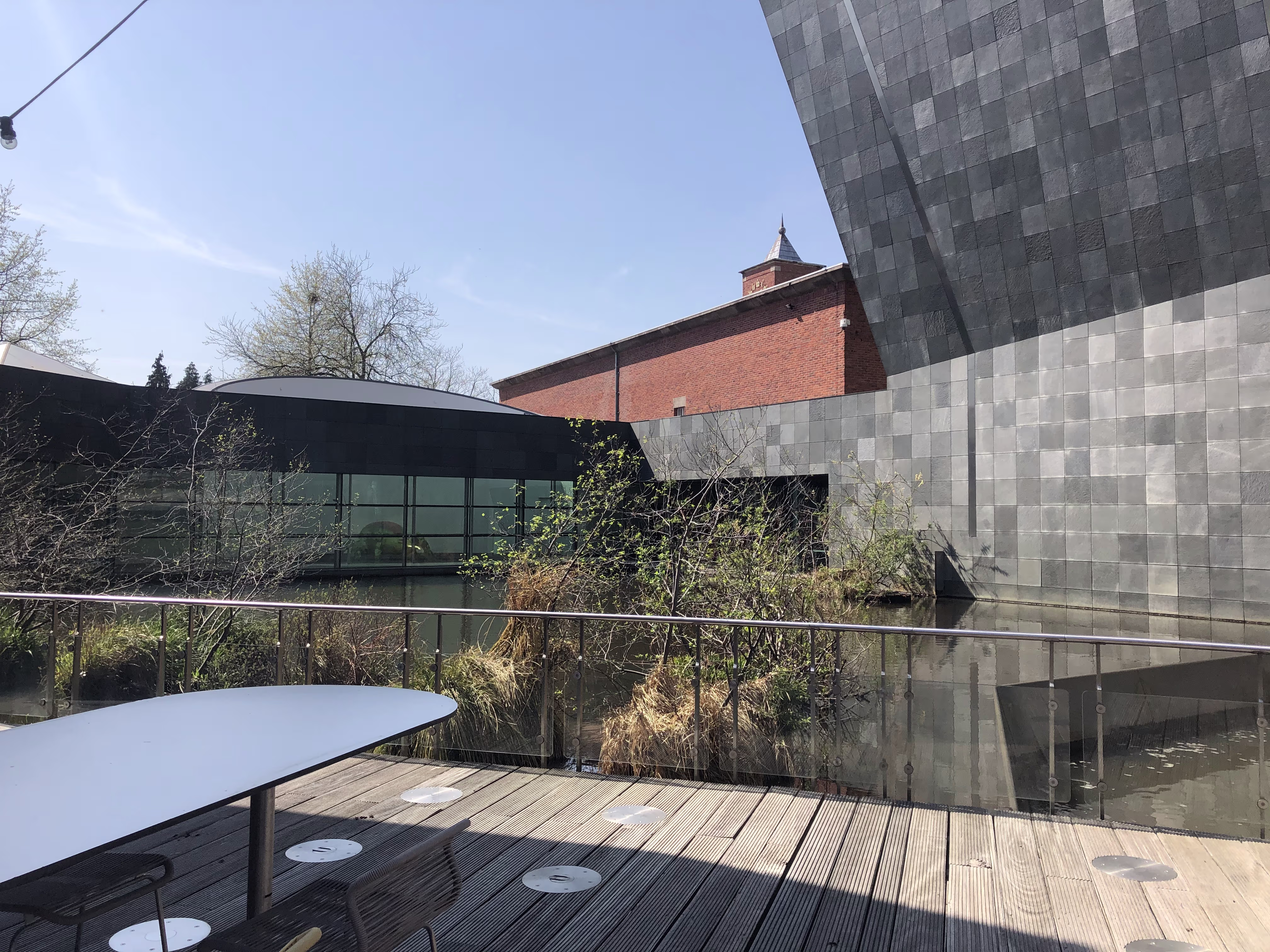 Moderne museumarchitectuur met glazen gevels en metalen panelen, gelegen naast een historisch bakstenen gebouw met toren.