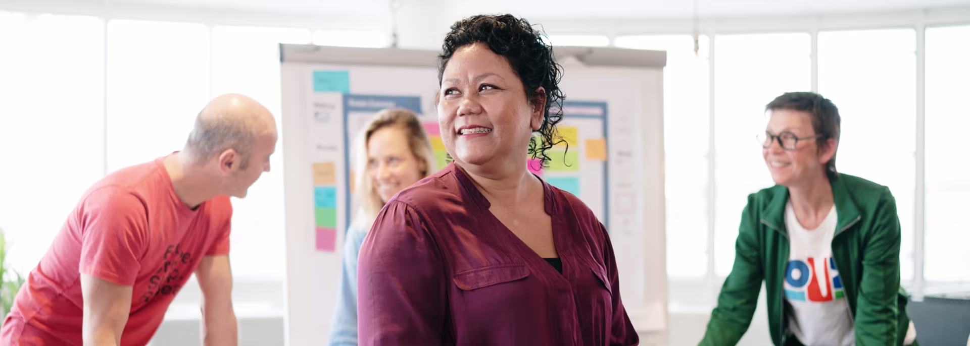 Vrolijke medewerkers van Gemeente Altena werken samen in een moderne kantooromgeving met whiteboards en post-its.