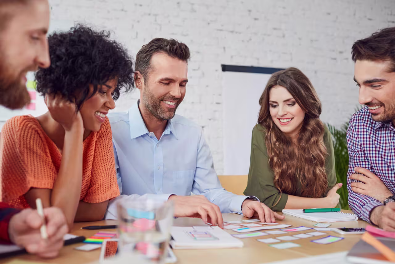 Een diverse groep collega's werkt samen aan een project met documenten en post-its op tafel in een moderne kantooromgeving.