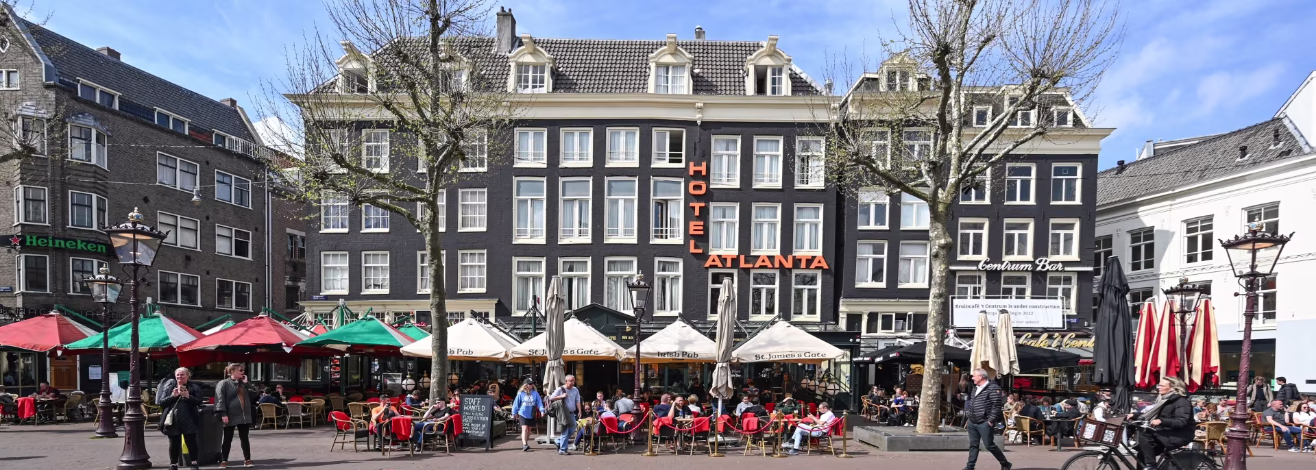 Gezellig stadsplein met historische gebouwen, terrasjse en mensen die ontspannen in de buitenlucht bij cafés en restaurants.
