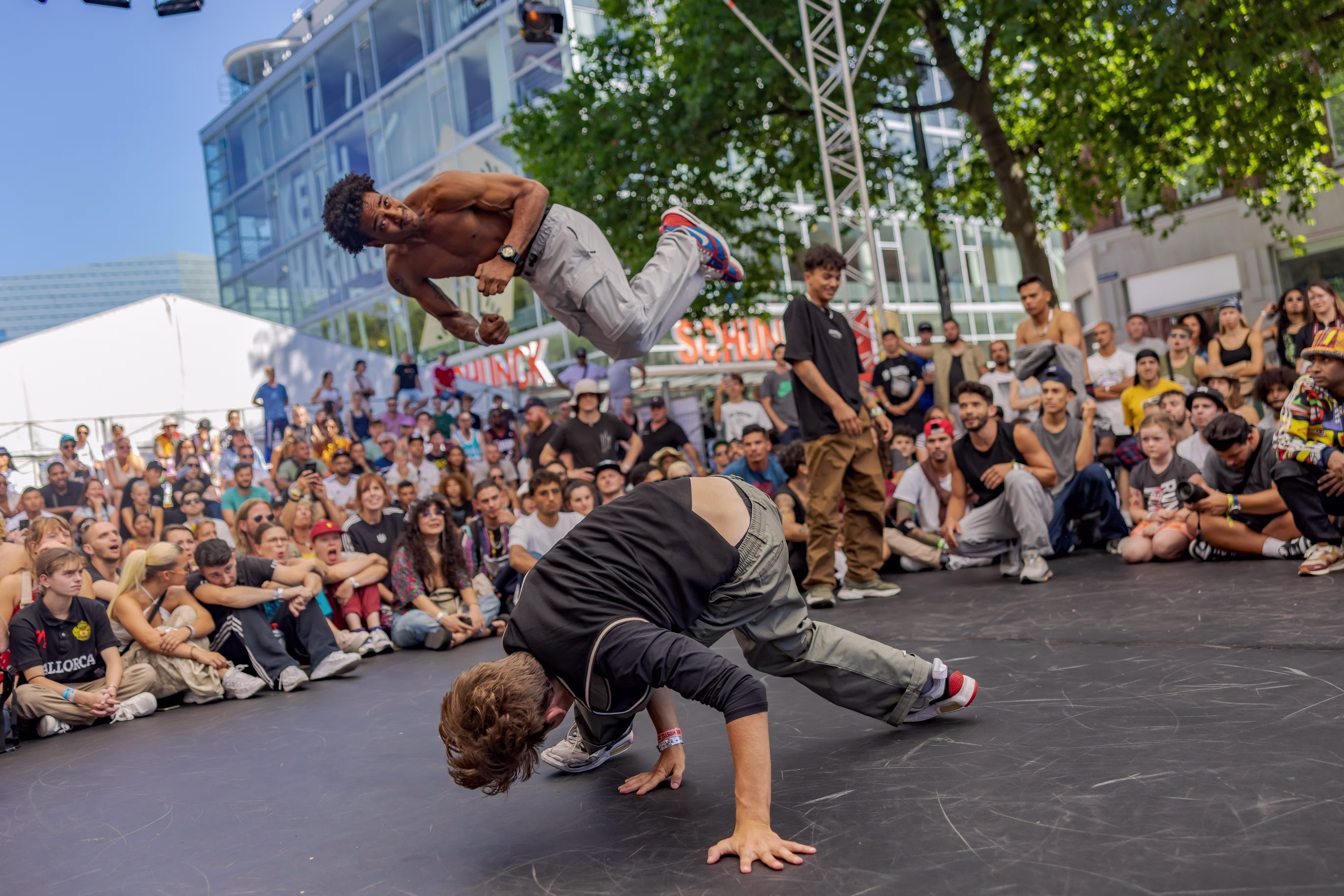 Breakdancers voeren acrobatische moves uit voor een grote zittende menigte tijdens een openlucht evenement.