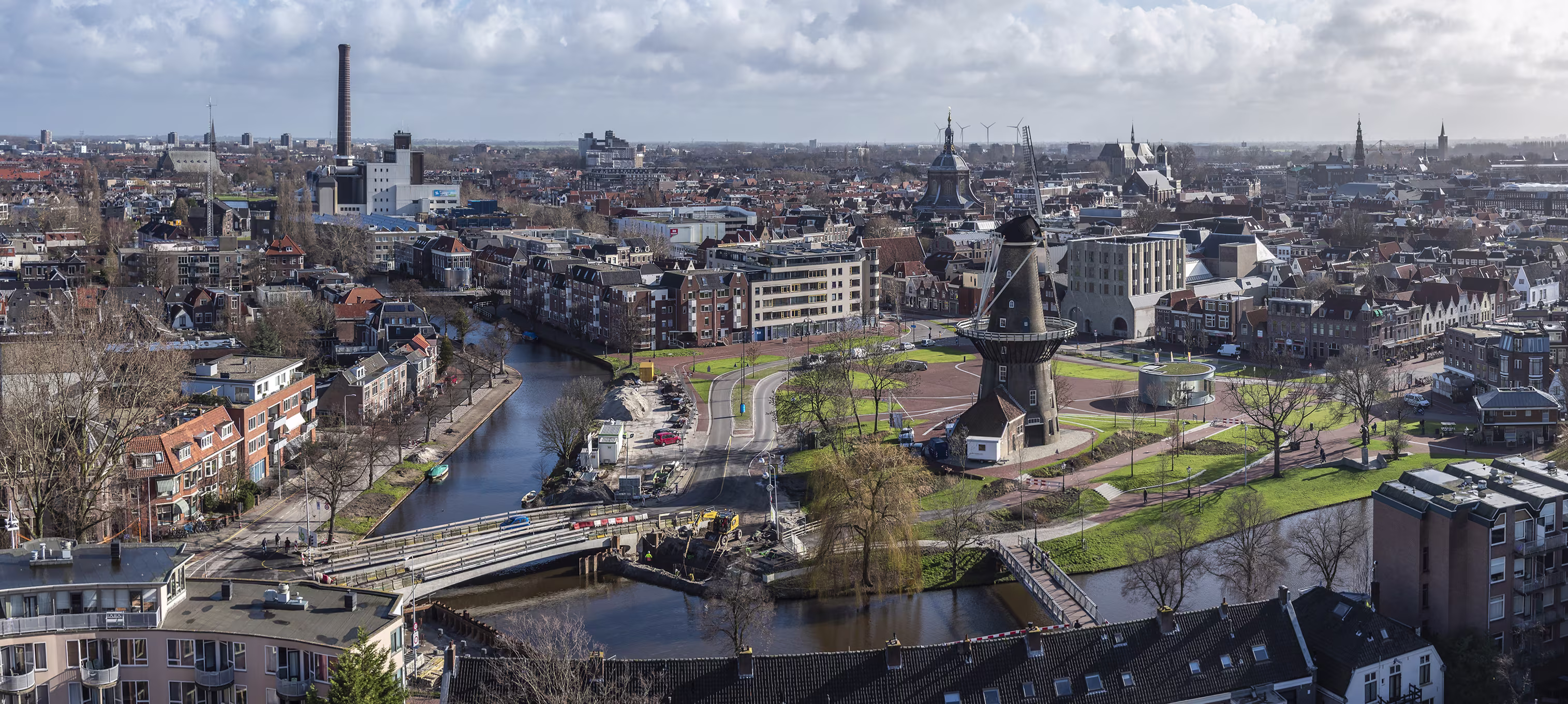 Luchtfoto van een Nederlandse stad met historische molen, rivier, brug en mix van oude en moderne gebouwen.