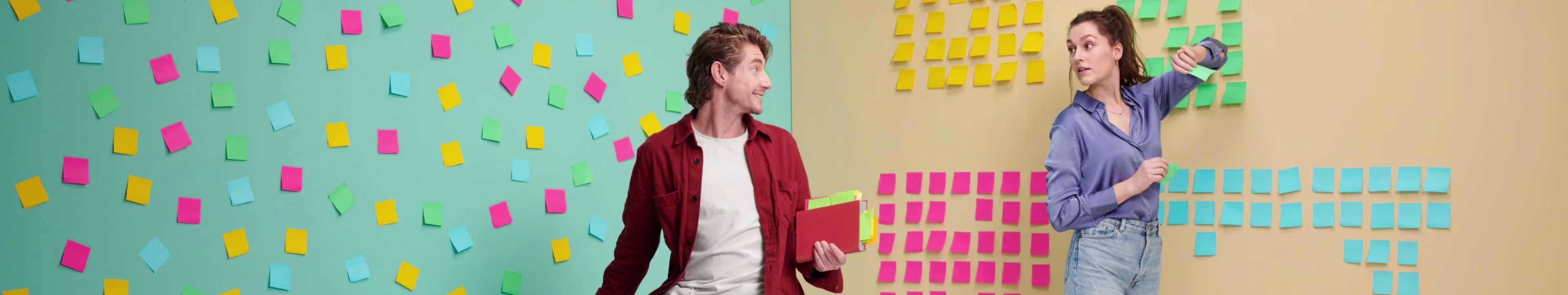 Twee vrouwen staan voor een muur vol gekleurde post-its en bespreken ideeën tijdens een brainstormsessie.