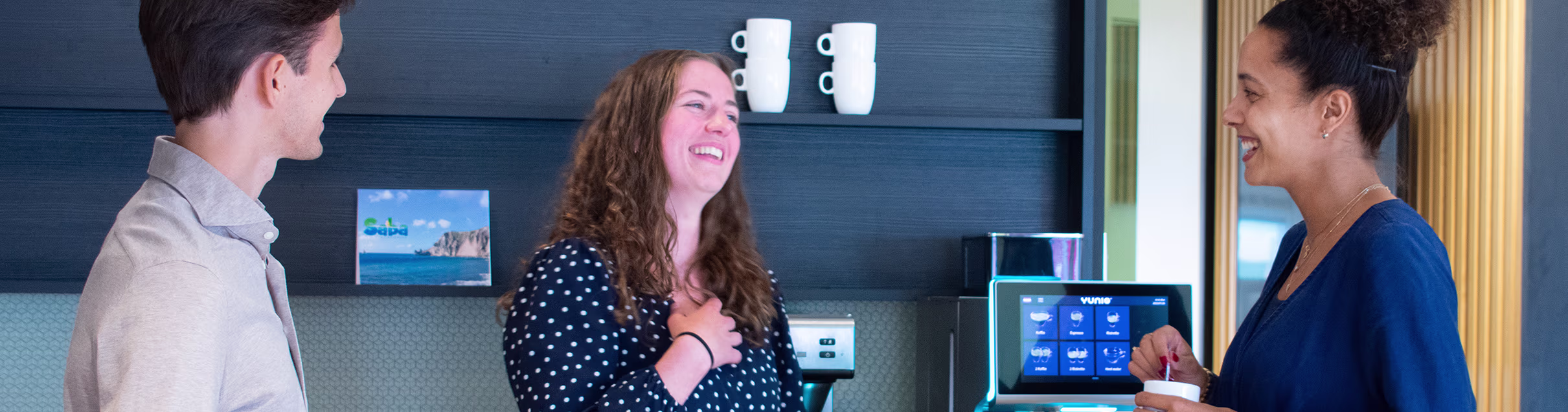 Drie collega's in gesprek bij een modern kantoor met schermen en digitale displays op de achtergrond.