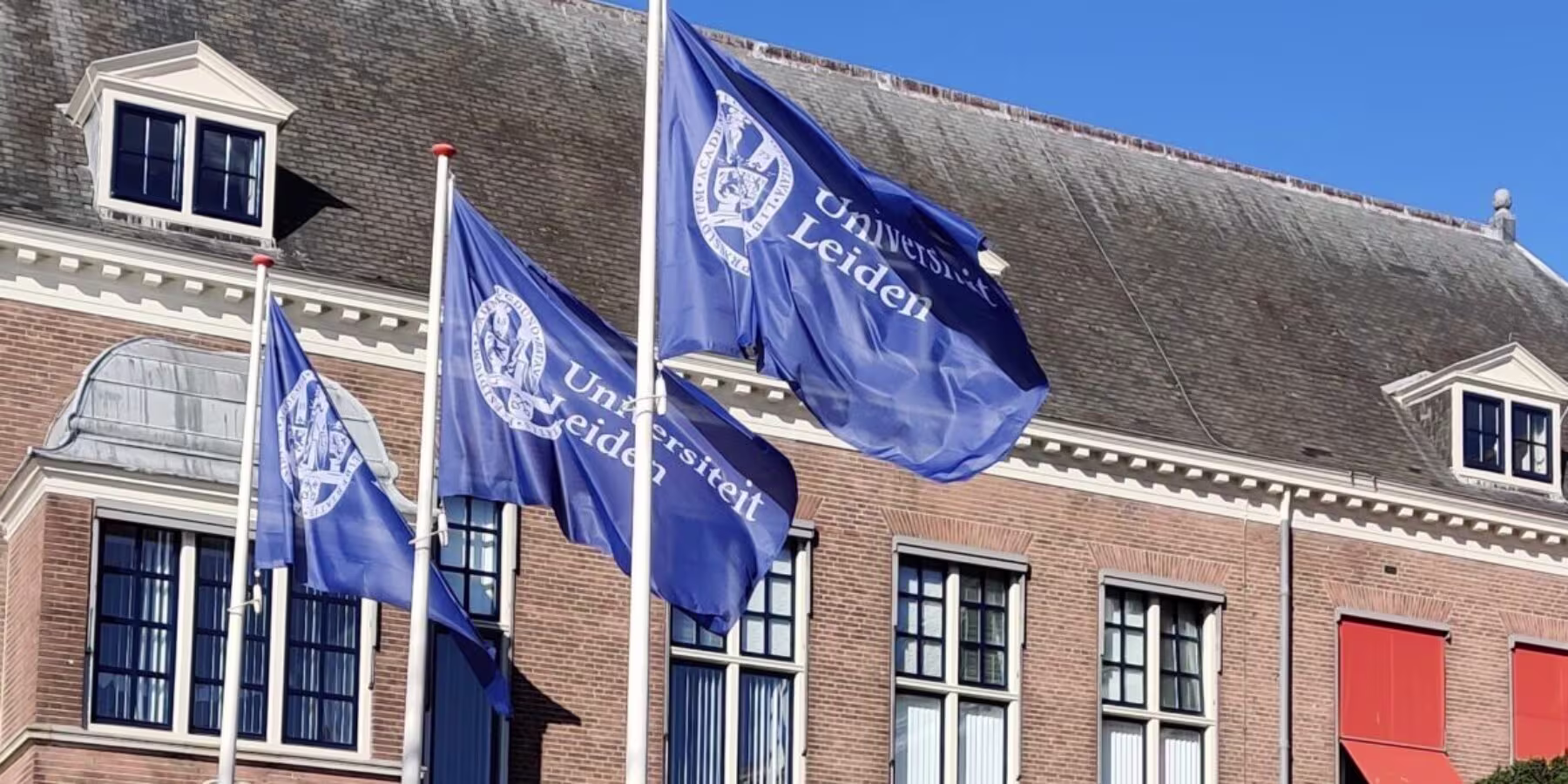Historisch universiteitsgebouw van Universiteit Leiden met drie blauwe vlaggen met het universiteitslogo.