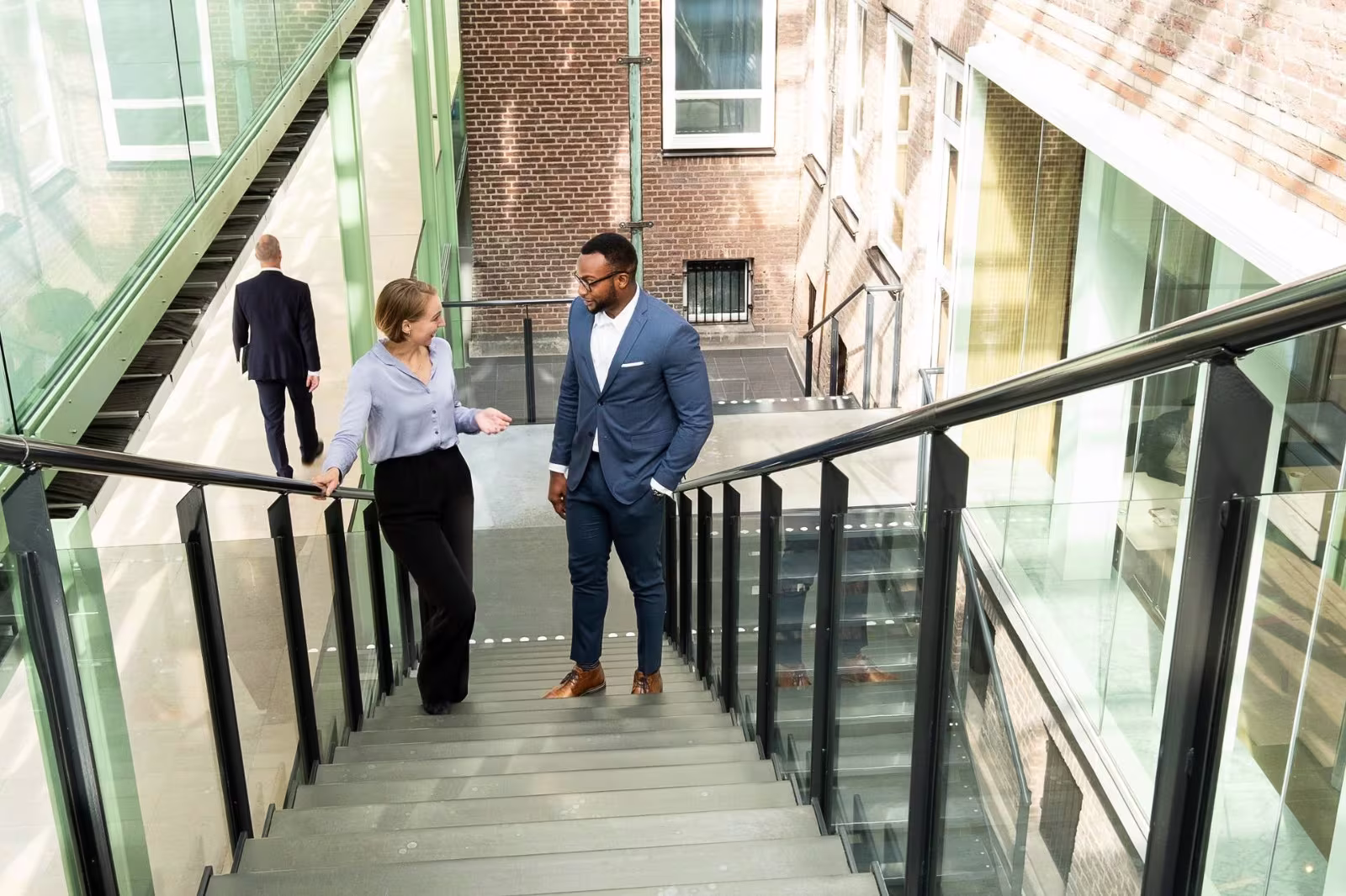 Twee professionals in zakelijke kleding lopen een moderne trap af in een glazen kantoorgebouw.