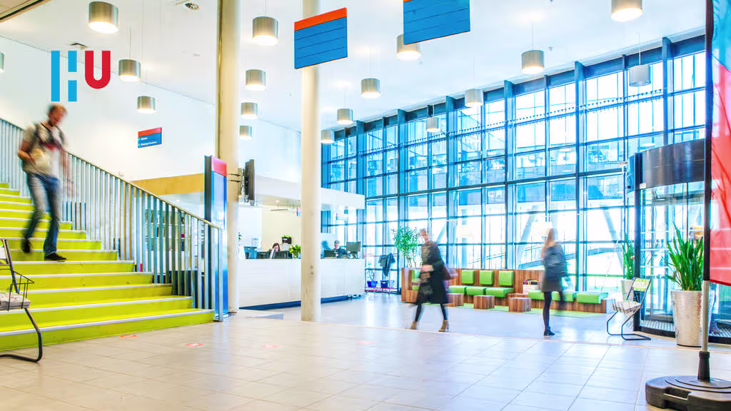 Moderne lobby van Hogeschool Utrecht met gele trap, grote ramen en mensen in beweging door de ruimte.