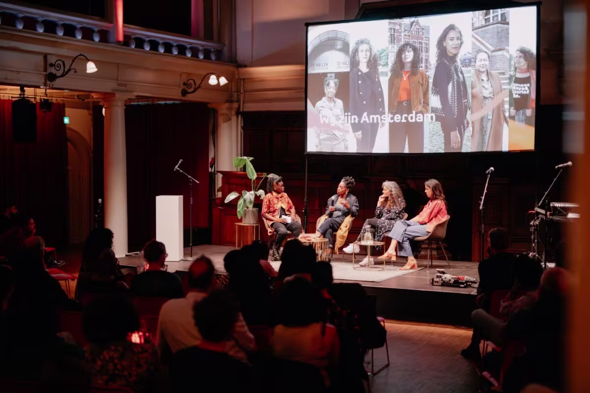Paneldiscussie op podium voor publiek in theaterzaal, met grote scherm op achtergrond waarop "Clip Amsterdam" staat.
