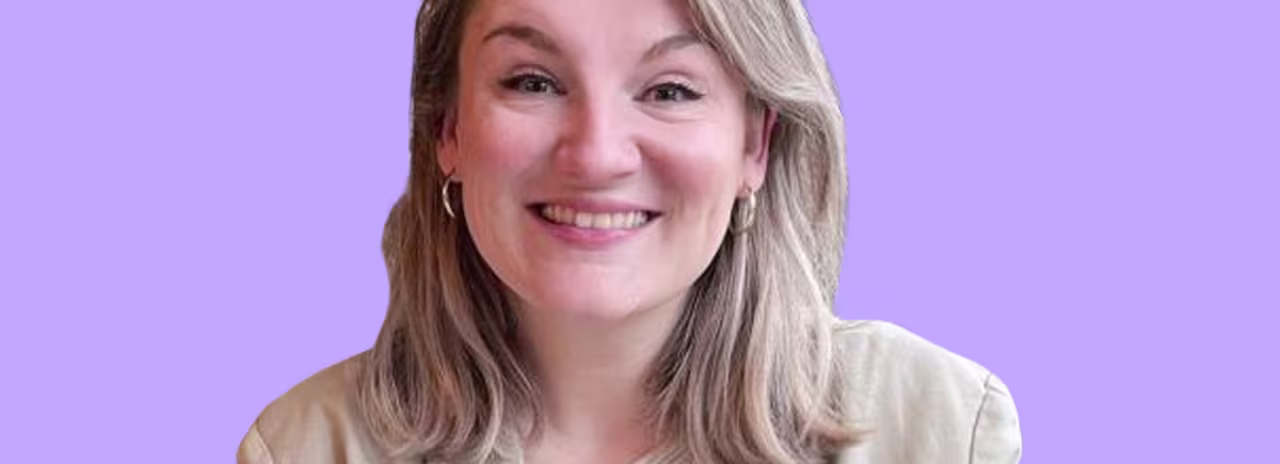 Glimlachende blonde vrouw in beige kleding tegen een lichtpaarse achtergrond, professionele portretfoto.