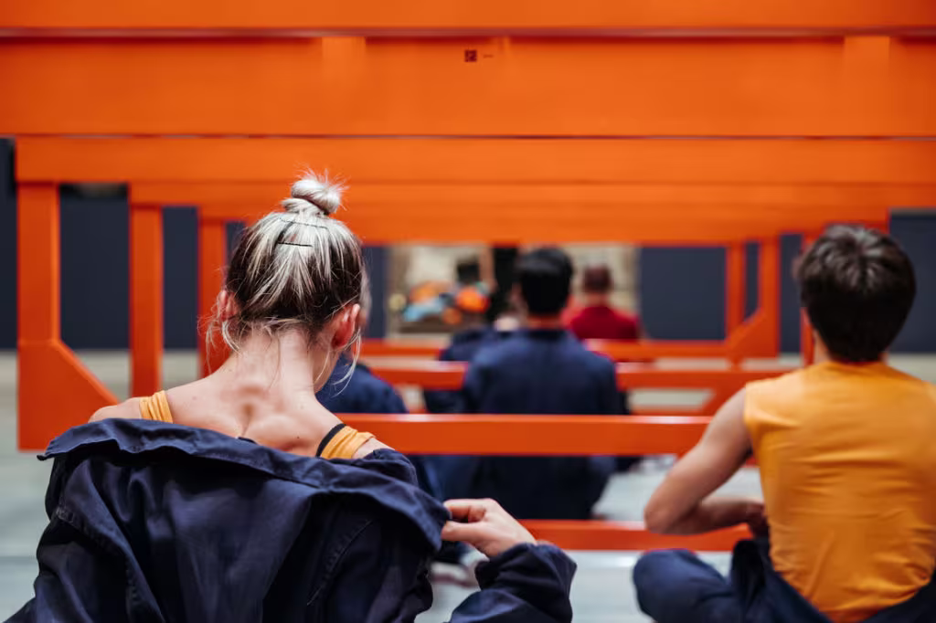 Mensen zitten op een bankje in een oranje treinstation en wachten op de trein.