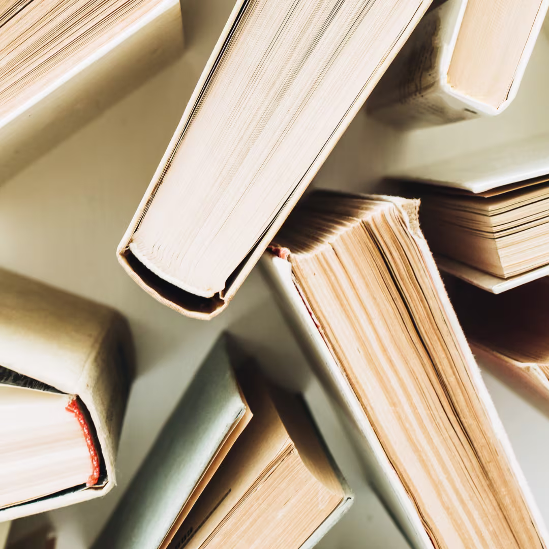 Een stapel opengeslagen boeken van bovenaf gefotografeerd, met zichtbare pagina's en warme belichting.
