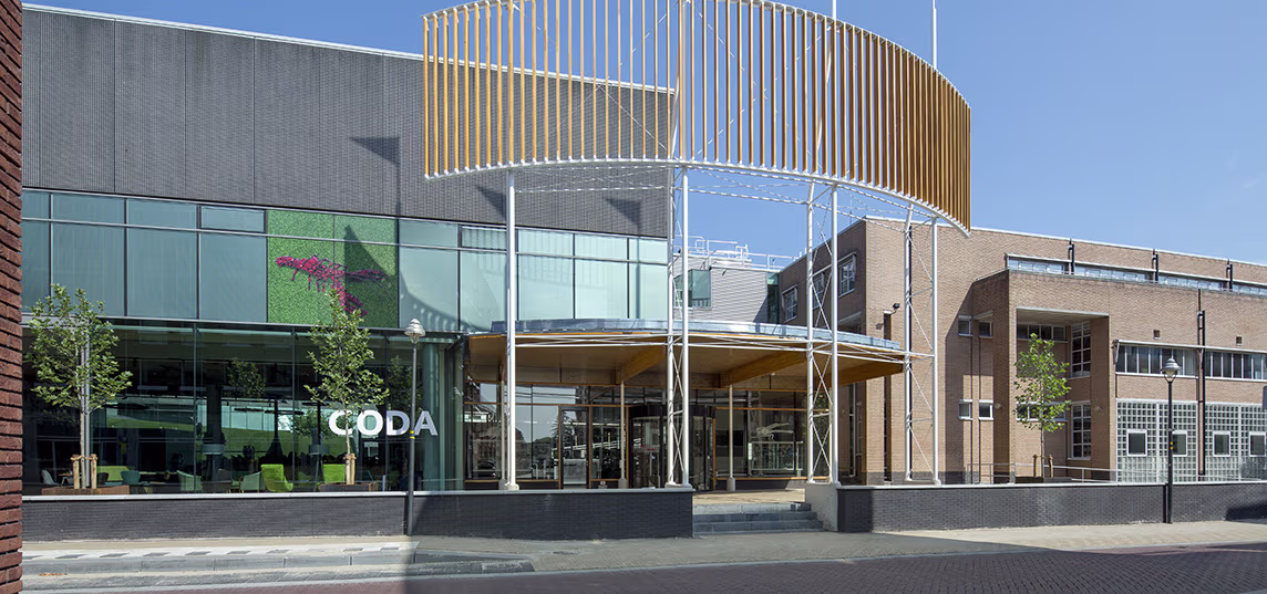 Modern cultuurgebouw van CODA met glazen gevel, houten lamellen en karakteristieke ronde vorm tegen blauwe hemel.
