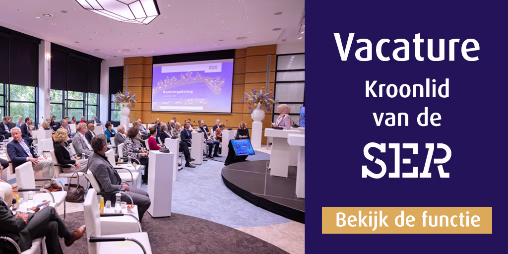 Vergaderruimte van de SER met publiek tijdens een bijeenkomst, spreker op podium met presentatiescherm op achtergrond.
