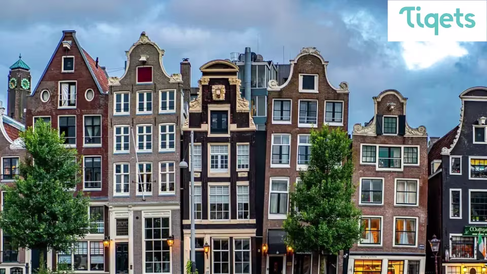 Historische Nederlandse grachtenpanden met karakteristieke gevels en groene bomen langs de straat onder bewolkte hemel.