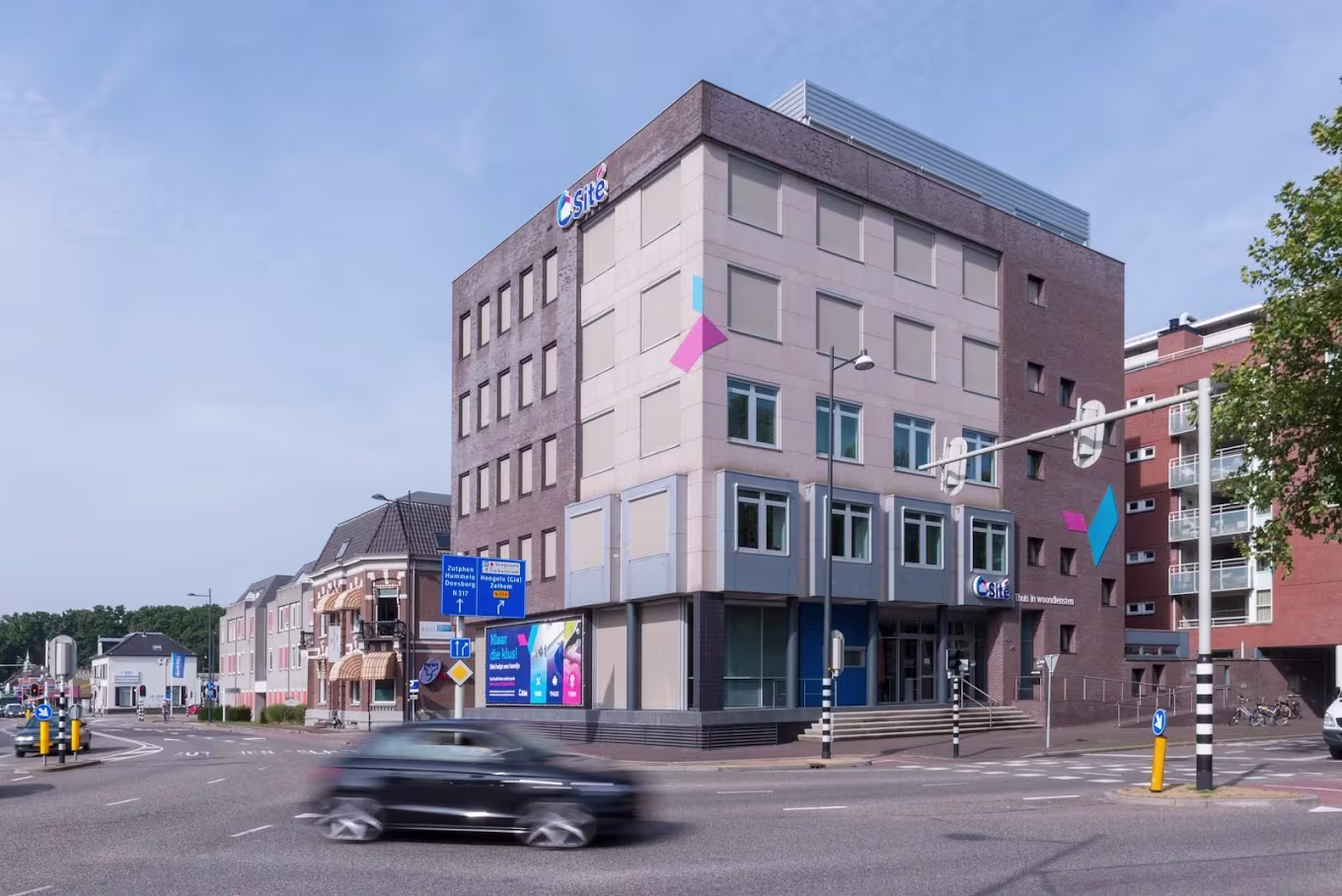 Modern gemeentehuis van Gemeente Altena met roze gevel en blauwe accenten, auto rijdt voorbij op straat.