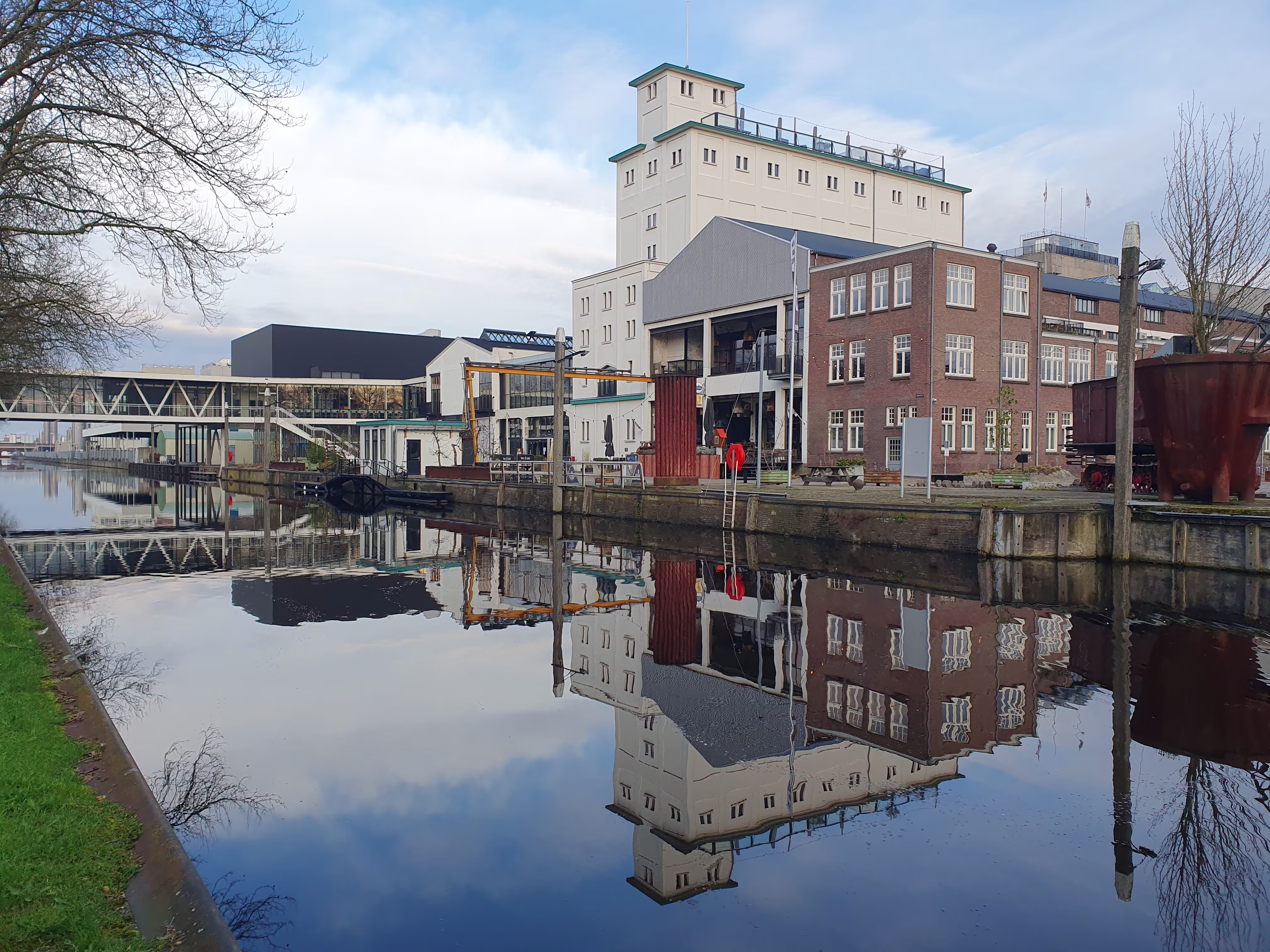 Historische industriële gebouwen aan het water met perfecte spiegeling, waaronder een hoge toren en bakstenen panden.