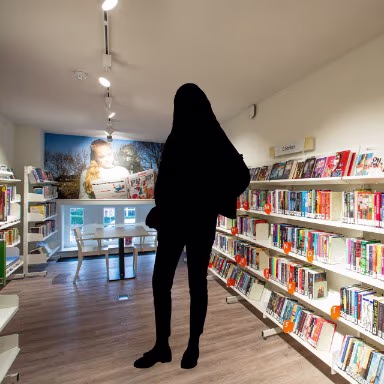 Een persoon bekijkt boeken in een moderne bibliotheek met witte boekenkasten en warme verlichting.