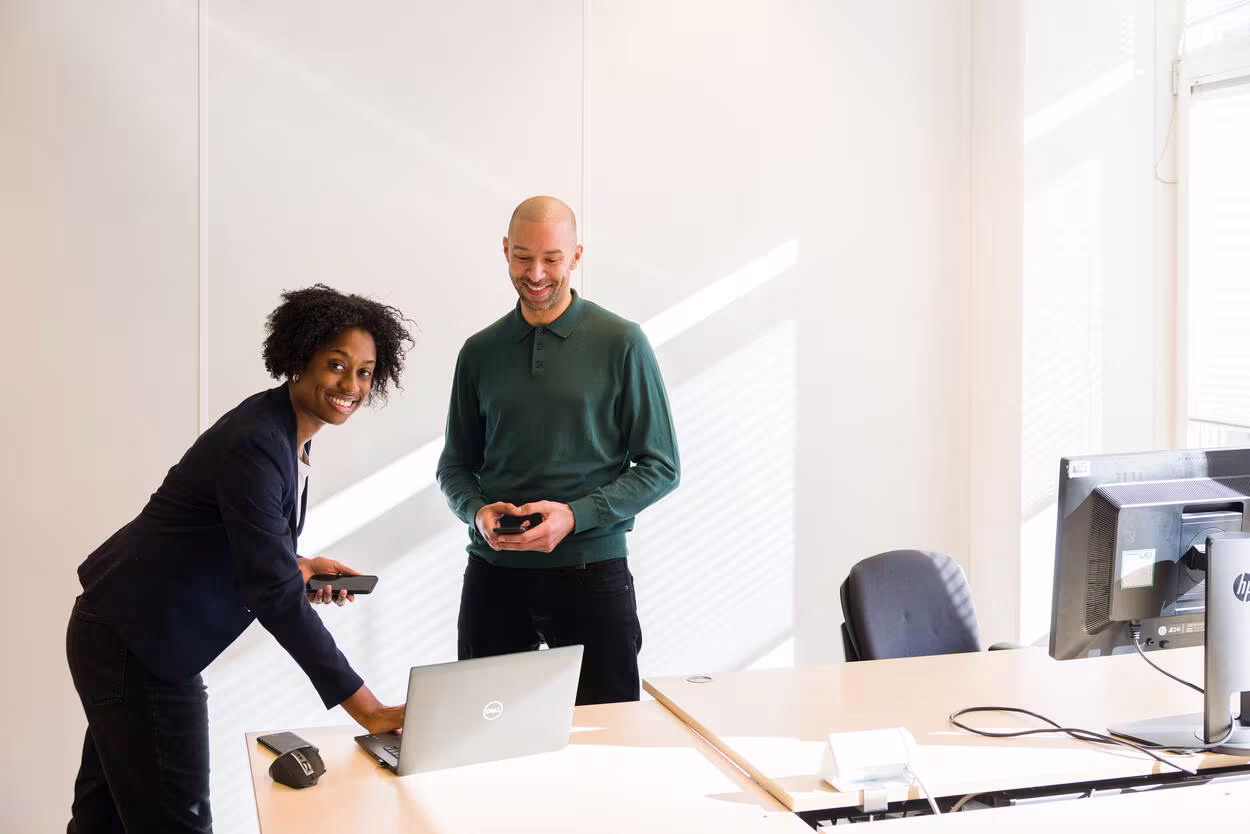 Twee collega's werken samen aan een laptop in een modern kantoor met veel daglicht.