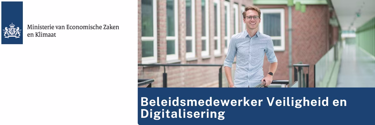 Een man in een blauw geruit overhemd staat glimlachend op een balkon voor een bakstenen gebouw met witte raamkozijnen.