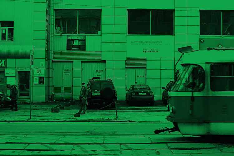 Een groene getinte straatfoto van een industrieel gebouw met auto's en mensen, wat een urbane werksfeer uitstraalt.