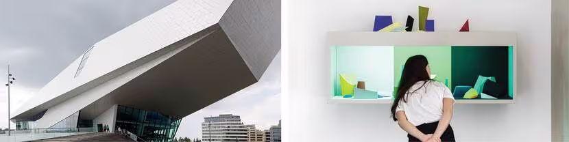 Modern wit gebouw met hoekige architectuur en een persoon die naar een kleurrijke wandinstallatie kijkt in een museum.