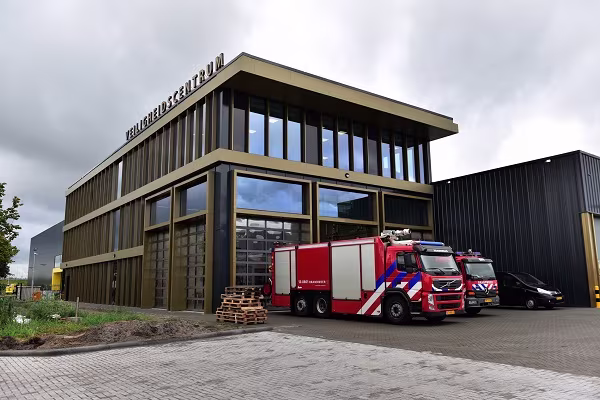 Een moderne brandweerkazerne met rode brandweerwagens geparkeerd voor het gebouw onder een bewolkte hemel.