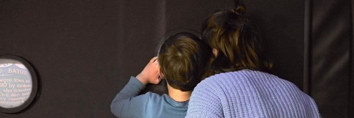 Twee personen bekijken samen een informatiebordje in een museum, van achteren gefotografeerd.