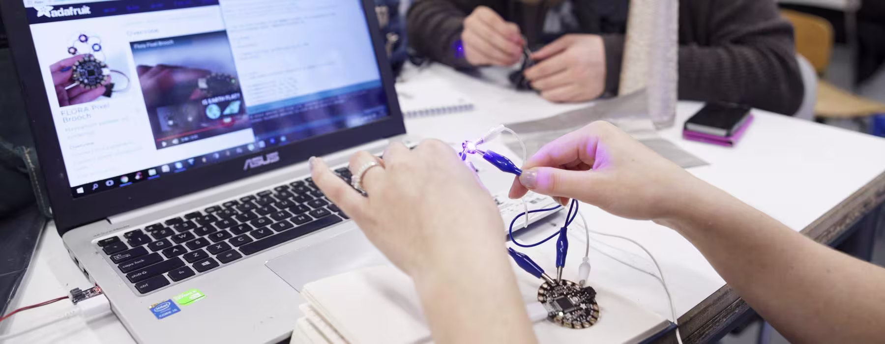 Student werkt aan elektronisch project met laptop en breadboard in technische onderwijsomgeving.