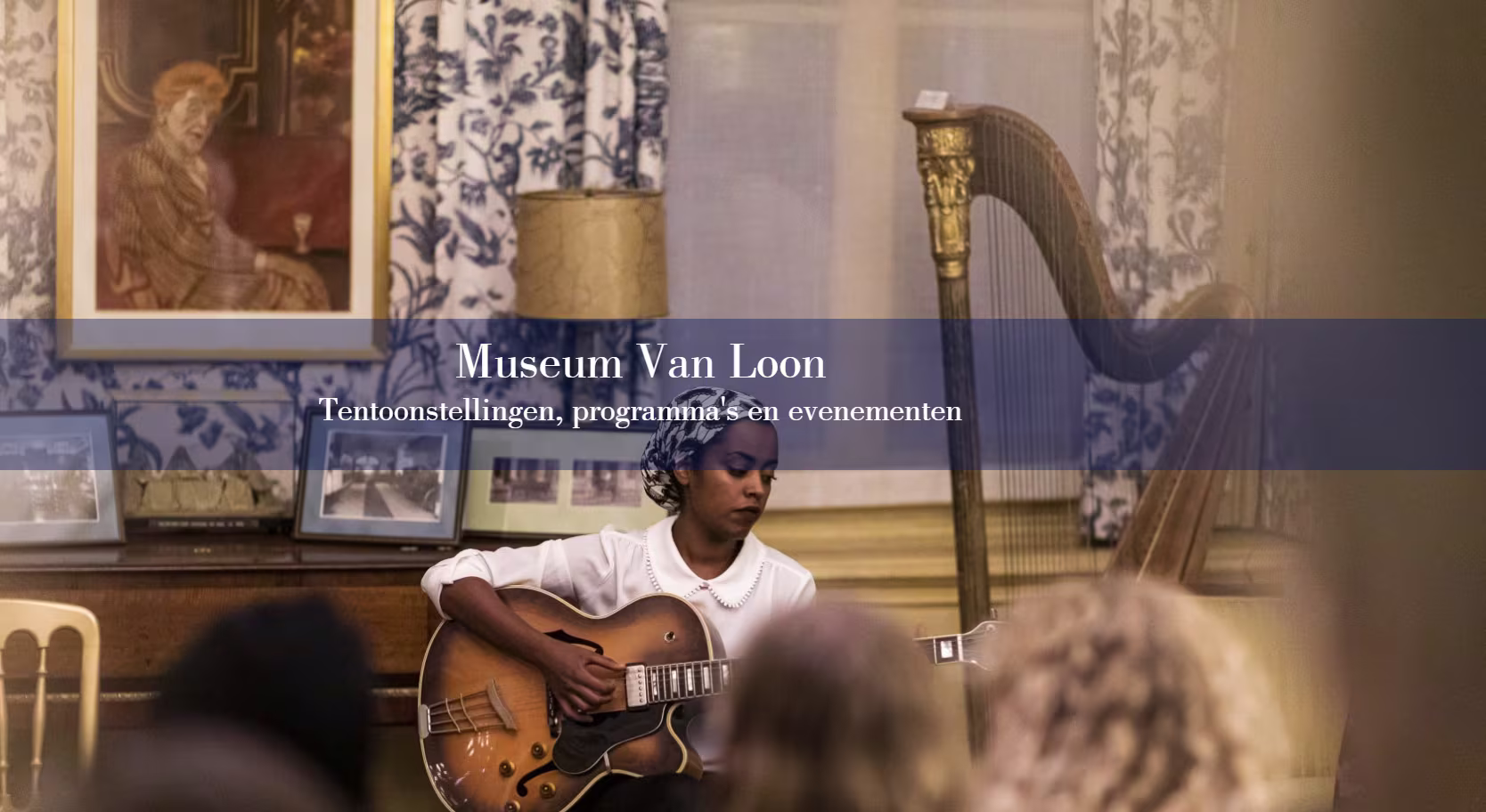Een muzikant speelt gitaar in een historische museumzaal met antieke instrumenten en schilderijen op de achtergrond.